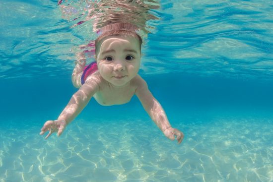 A baby (five month old, Isabella Mustard) swims underwater in the ocean. Seven Mile Beach, Grand Cayman, Cayman Islands, British West Indies. Caribbean SeaDigital manipulated - parts of mother removed. Model Released.