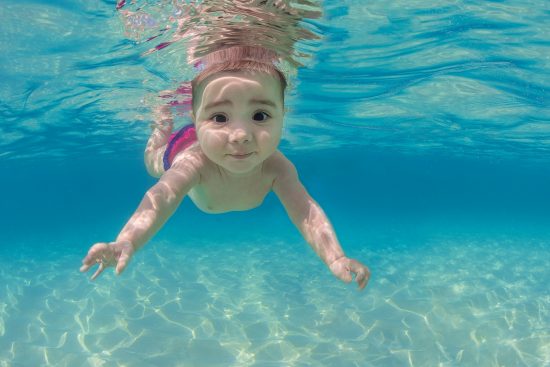 A baby (five month old, Isabella Mustard) swims underwater in the ocean. Seven Mile Beach, Grand Cayman, Cayman Islands, British West Indies. Caribbean Sea
Digital manipulated - parts of mother removed. 
Model Released.